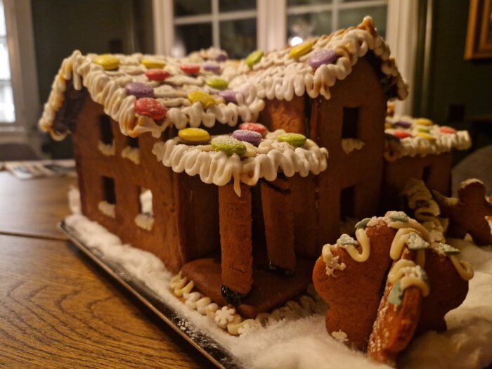 Pepparkakshus dekorerat med kristyr och godis, modell av någons hem, på ett bord med snöliknande underlag.