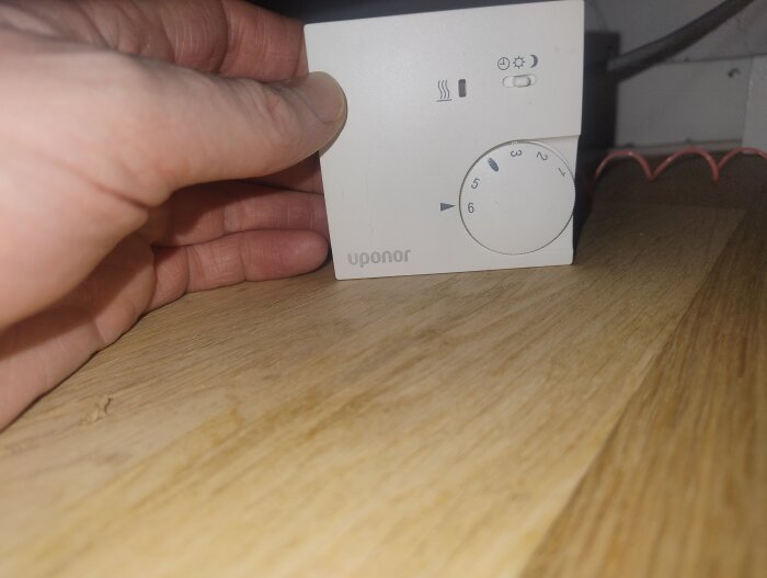 Hand håller en Uponor-termostat på ett träbord.