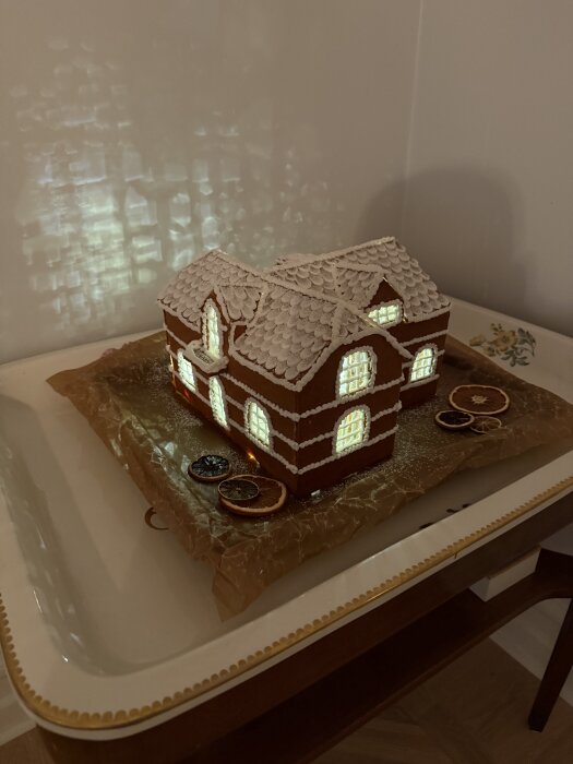 Pepparkakshus med belysning, byggt som en modell av ett sekelskifteshus med vinklade tak och flera husdelar, placerat på en bricka.