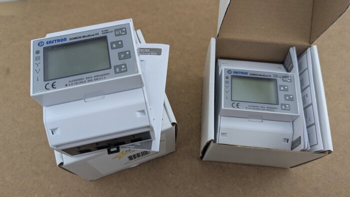 Två oanvända Eastron SDM630 Modbus MID V2 elmätare i sina förpackningar på ett bord.