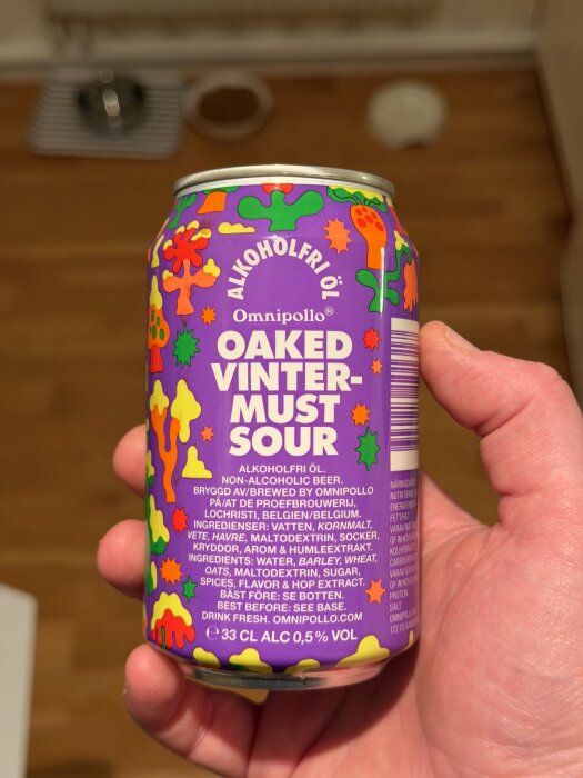 Lila burk med färgglada mönster som innehåller alkoholfri öl från Omnipollo, kallad "Oaked Vinter-Must Sour", hålls i en hand.