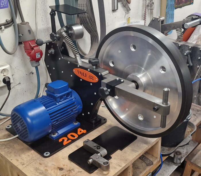 Bandslip med 500 mm kontakthjul och blå motor på ett verkstadsgolv. Märken: Claryx Metalworks och Volf48grinders.