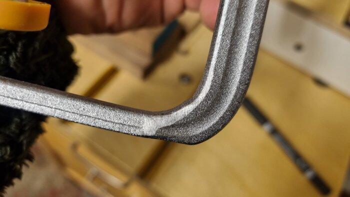 Närbild av en metalltving som visar böjen där profilen nästan passar i skenan, med handen delvis synlig i bakgrunden.