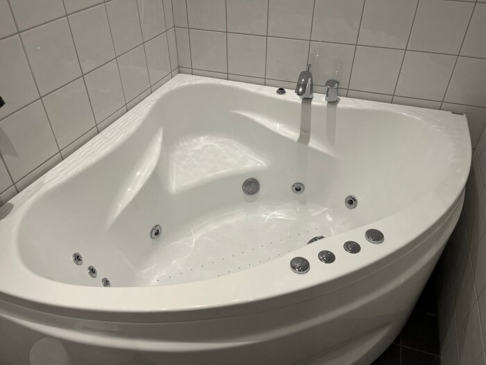 Bubbelbadkar i hörnet av ett kaklat badrum, märkt "PoolSpa", med flera jetmunstycken och kranar, saknar eventuellt duschmunstycke.
