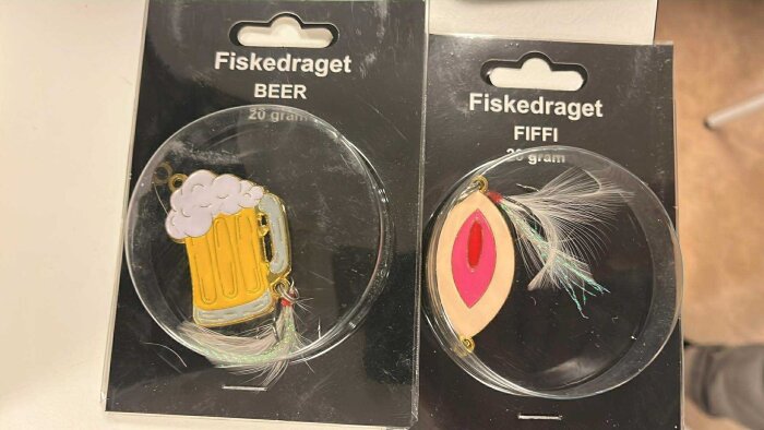 Förpackningar med två fiskedrag: ett i form av en ölsejdel och ett i form av en dekorativ fjäder med röd detalj.