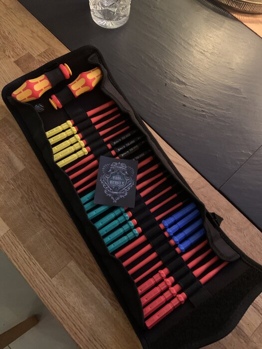 Verktygsset med färgglada isolerade skruvmejslar i en öppen verktygsväska på ett bord.