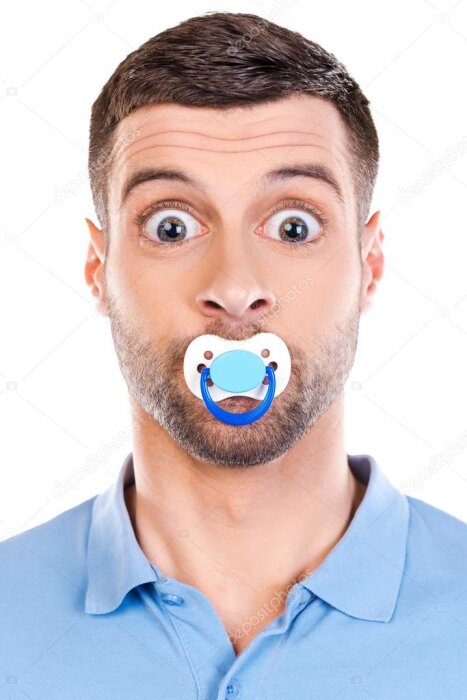 Man med skägg i blå pikétröja har en napp i munnen och ser förvånad ut.