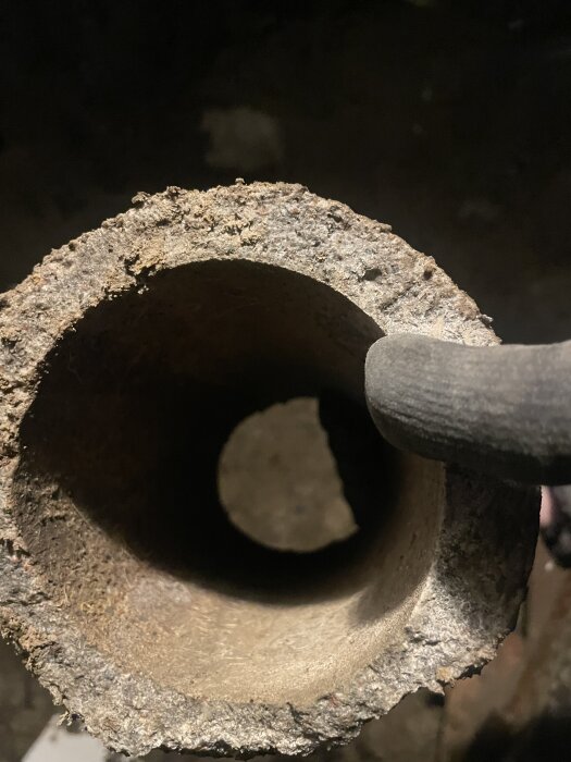 Närbild av änden på ett grovt betongrör som grävts fram, med en hand som håller röret för inspektion.