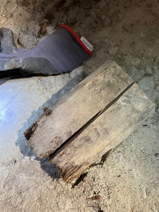 Ruttet träbit och en handske på ett betonggolv med sprickor och smuts från ett renoveringsprojekt.