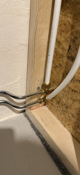 Vattenrör kopplade med mässingsfördelare och monterade i träregel mot en OSB-skiva.