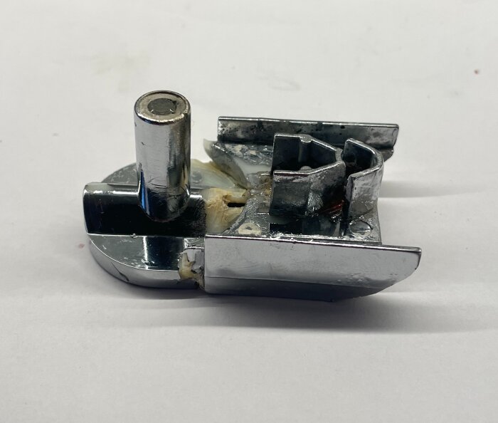 Defekt duschväggsfäste i metall med skadade delar, placerat på en vit bakgrund.