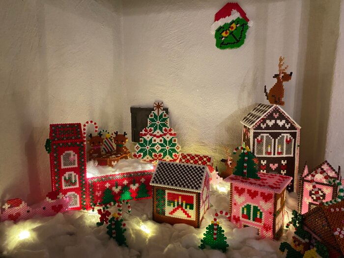 Pärlplattebygge av julby med hus, ren och granar, omgivna av små ljusslingor och vit "snö".