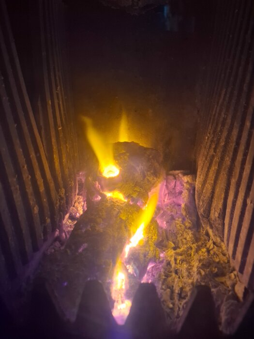 Brinnande ved i en öppen spis med intensivt gula lågor och glödande vedbitar, omgivna av mörka, sotiga väggar.