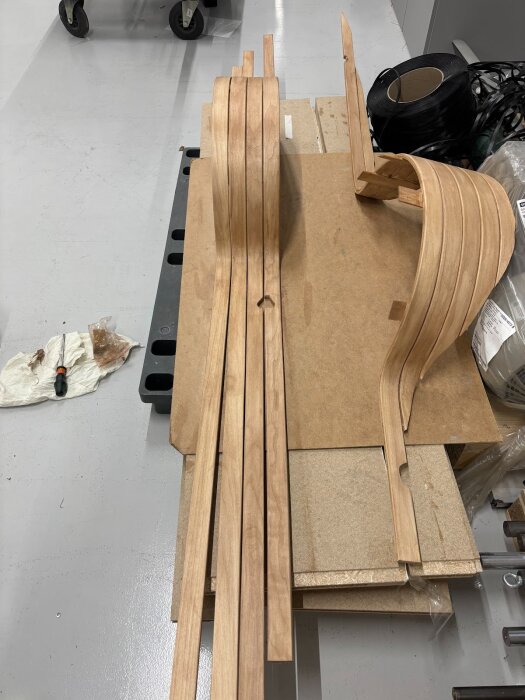 Böjda träbågar och brädor på arbetsbänk för golvprojekt, omgivet av verktyg och rullar med svart material.