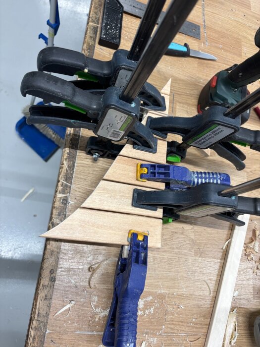 Träbitar hålls samman med tvingar på en arbetsbänk, en del av ett pågående golvprojekt med bastuvaxade delar och silikonlimning.