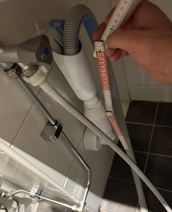 Mätning av avloppsrör vid installation av tvättmaskin och torktumlare, med slangar och verktyg synliga.