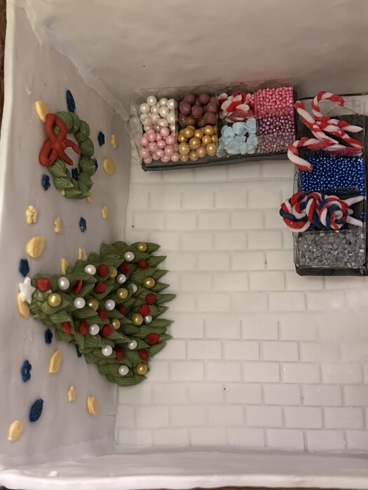 Pepparkakshus med små godisbutiker, dekorerat med olika sorters färgglada godisar och en grön krans på väggen.