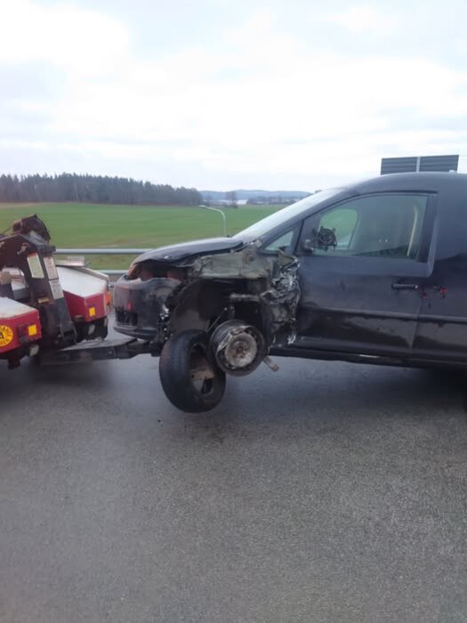 Svart skåpbil med skadad front, bogseras bort efter en trafikolycka på landsväg.