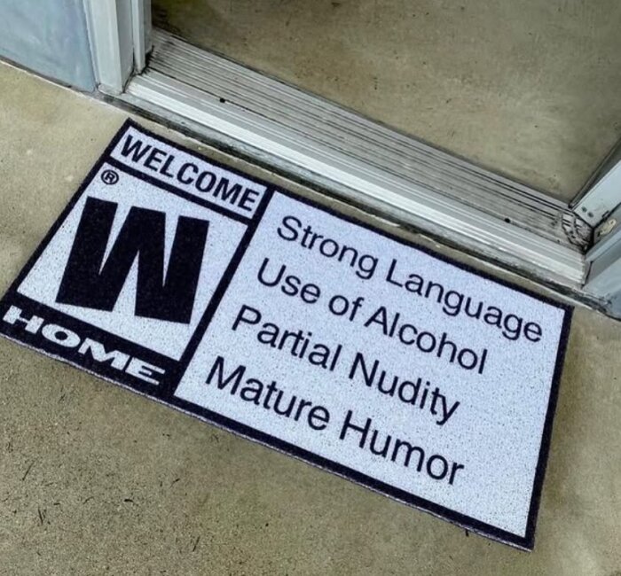 Dörrmatta vid ingång med text: "WELCOME HOME; Strong Language, Use of Alcohol, Partial Nudity, Mature Humor".