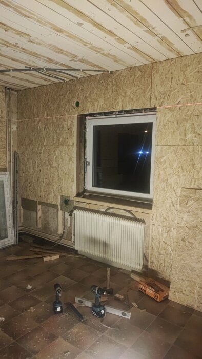 Rum under renovering med ett nytt fönster monterat, synliga verktyg och oskyddad innervägg av spånskiva.