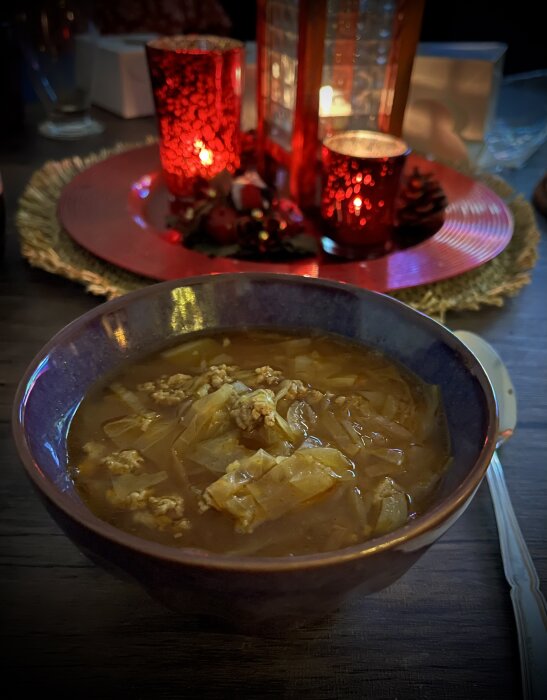 Skål med Nikkaluoktasoppa på ett bord, omgiven av röda ljus och dekorationer.