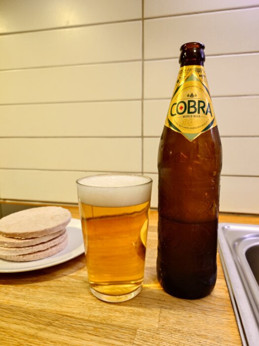 Flaska och glas med öl på köksbänk bredvid en tallrik med tunnbröd.