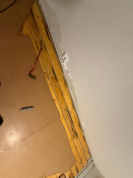 Uppbrutet golv i gillestuga, synligt trägolv och äldre byggmaterial. Kofot och kniv syns vid arbetsområdet.