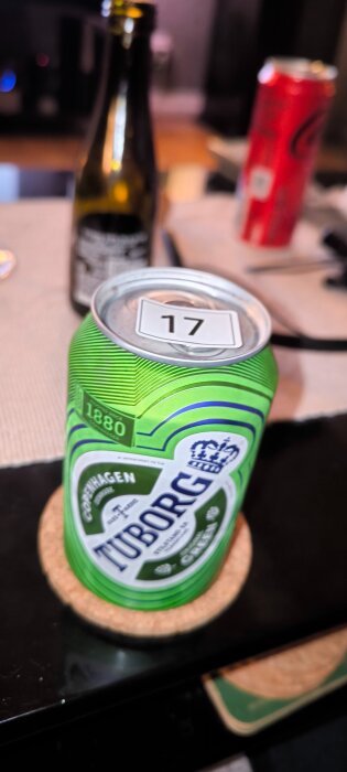 Grön dryckesburk med etiketten Tuborg på ett bord; nummer 17 på burkens öppning. I bakgrunden en flaska och en röd burk.