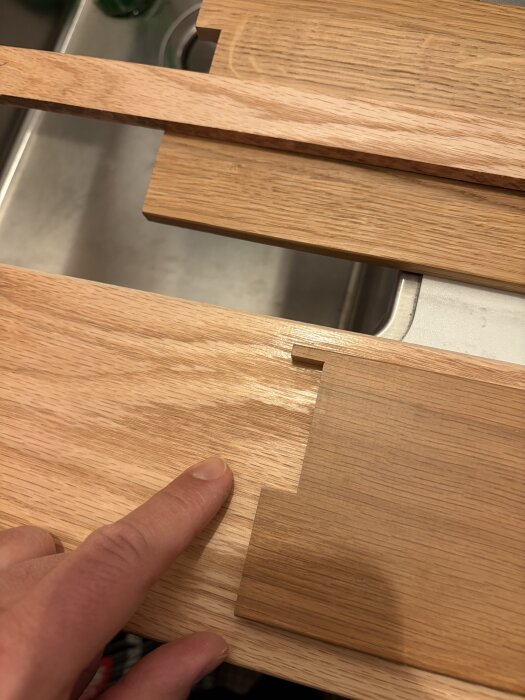 Finger pekar på en urtagning i tröskel av trä vid köksbänk, med fokus på hyvlad kant.