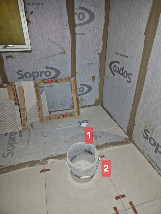 Badrumsrenovering med fokus på kuvertskärning kring golvbrunn, där golvplattor och fogar är markerade framför en dusch under konstruktion.