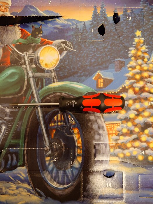 Julkalenderbild med en illustration av en figur på motorcykel med en katt och en skruvmejsel ovanpå kalendern. Snöscen med stuga och julgran.