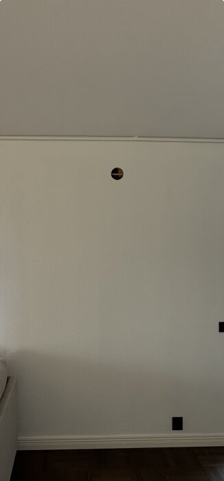 Ett stort hål i en vit vägg, med en balk synlig bakom hålet. Väggen behöver lagas där hålet för en planerad ventil togs upp.