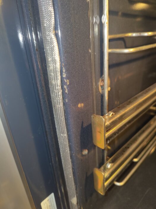 Ugnen med skadad emalj i framkant, visar blottat metallområde nära ugnsstång.