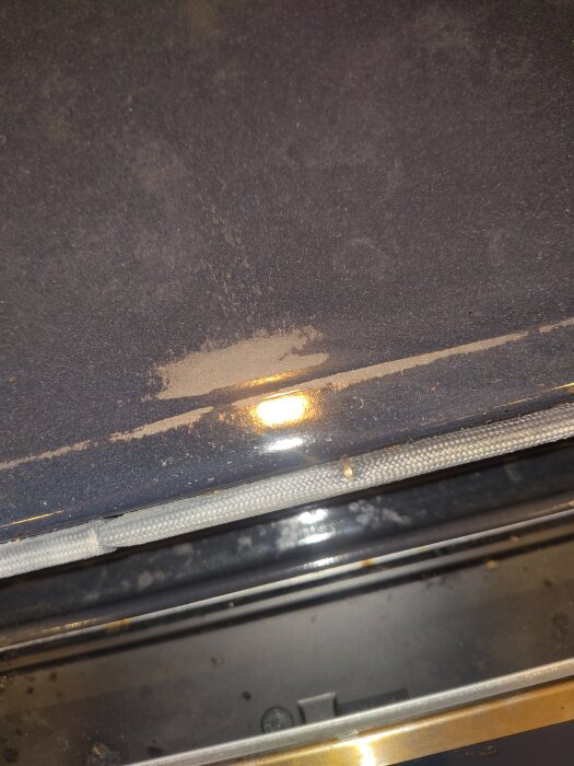 Skadad emalj i en Bosch inbyggnadsugn, med flera hål som visar blottad metall i framkanten. Ugnen är av pyrolystyp.