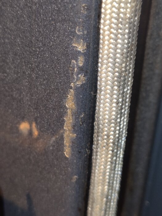 Detaljbild av skadad emalj i en Bosch inbyggnadsugn, där metallen syns igenom tillsammans med en flätad tråd längs kanten.