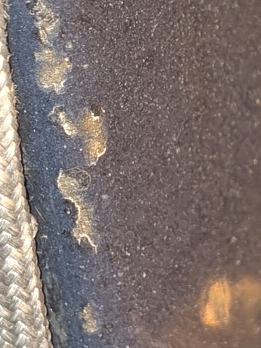 Närbild av skadad emalj på ugnens framkant där metallen är synlig genom flera hål och repor.
