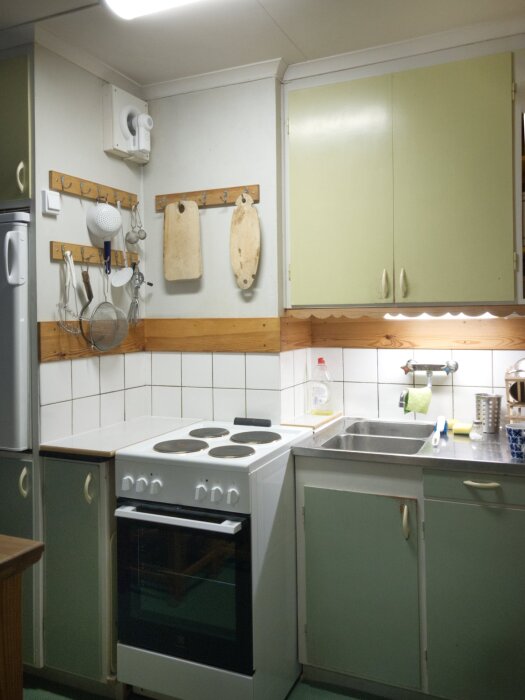 Kök med grön inredning från 1960-talet, ny fläkt och 50 cm spis, bredvid brickfack och diskbänk, LED-belysning under skåp.