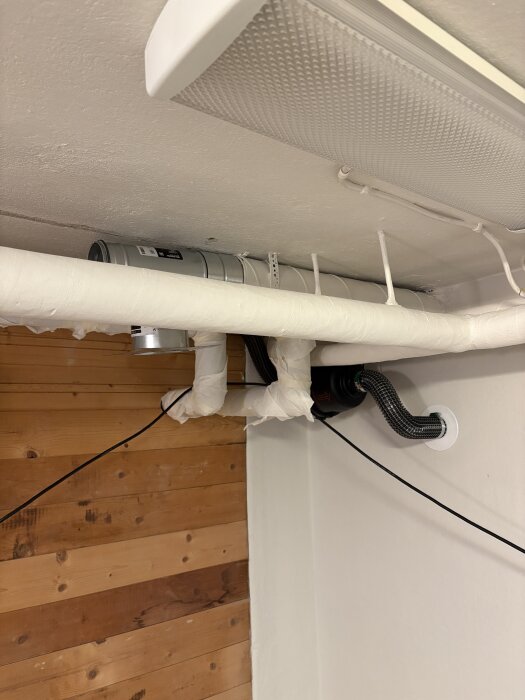 T-rör med pax-fläkt monterat i taket med rörisolering och elkabel, närbild i renoveringsprojekt.