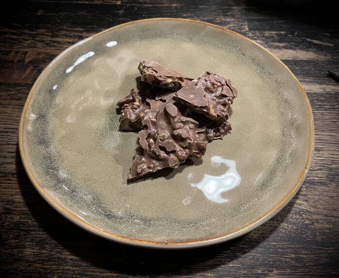 Hemgjort nötbräck med choklad, pistagenötter och valnötter på ett beige fat.