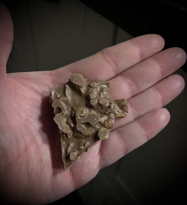 Hand håller en bit nötbräck med choklad, pistagenötter och valnötter.