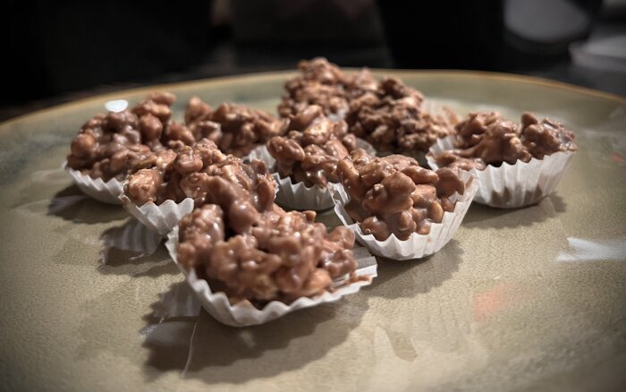 Hemgjorda chokladbitar med apelsinkrokantschoklad, rispuffar och flingor i pappersformar på ett fat.