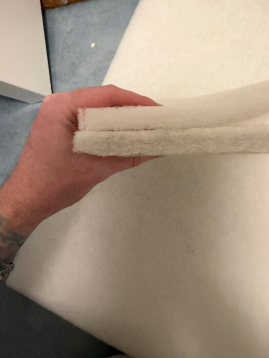 En hand håller ett lager av vit G3-klassat filtermaterial, redo att klippas till rätt storlek.