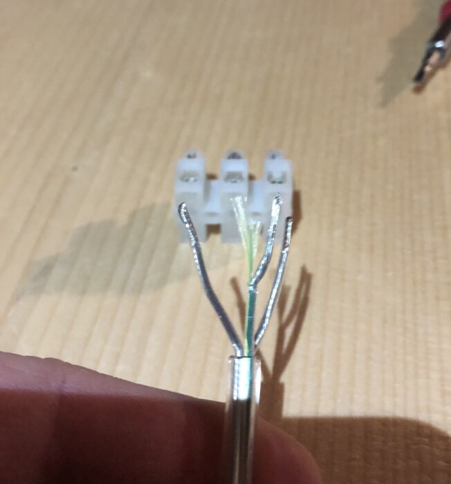 Elektriska kablar skalade och delade i fyra leder framför en kopplingsplint på ett träbord.