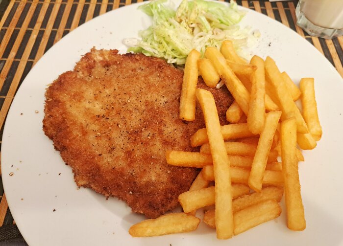 Schnitzel med pommes frites och sallad på en vit tallrik.