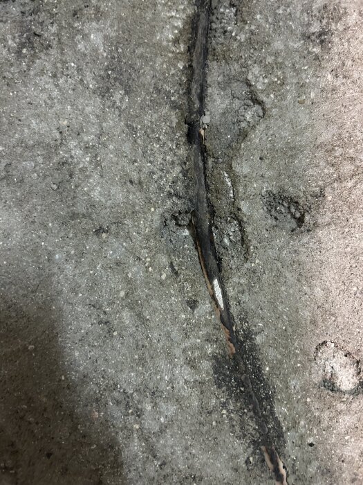 Vattenrör i betonggolv visar djup skada efter slipning under sanering av badrum.