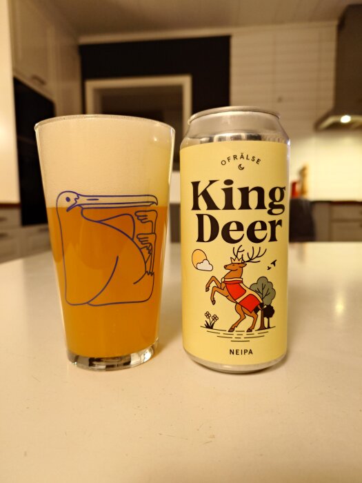 Ett glas med skummande öl bredvid en burk märkt "King Deer NEIPA" på ett köksbord.