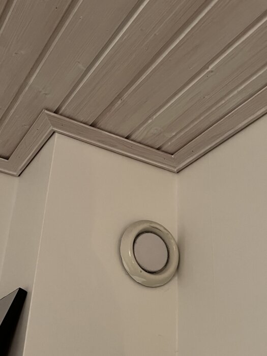 Trätak och hörnvägg med en rund ventil i beige.