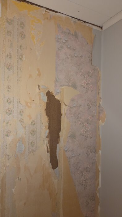 Avskavd tapet med olika mönsterlager på en vägg under renovering, avslöjar blommiga och randiga motiv.