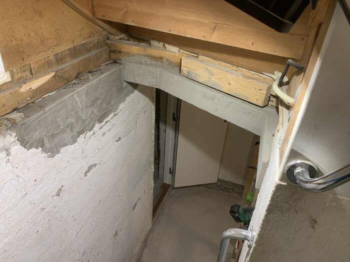 Invändig källarnedgång med trästomme och betongväggar, nyrenoverad och betsad, sett från ovan med en dörr i bakgrunden.