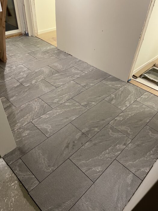 Nylagt grått klinkergolv i en hall under renovering, med synliga dörröppningar och en vitmålad vägg.